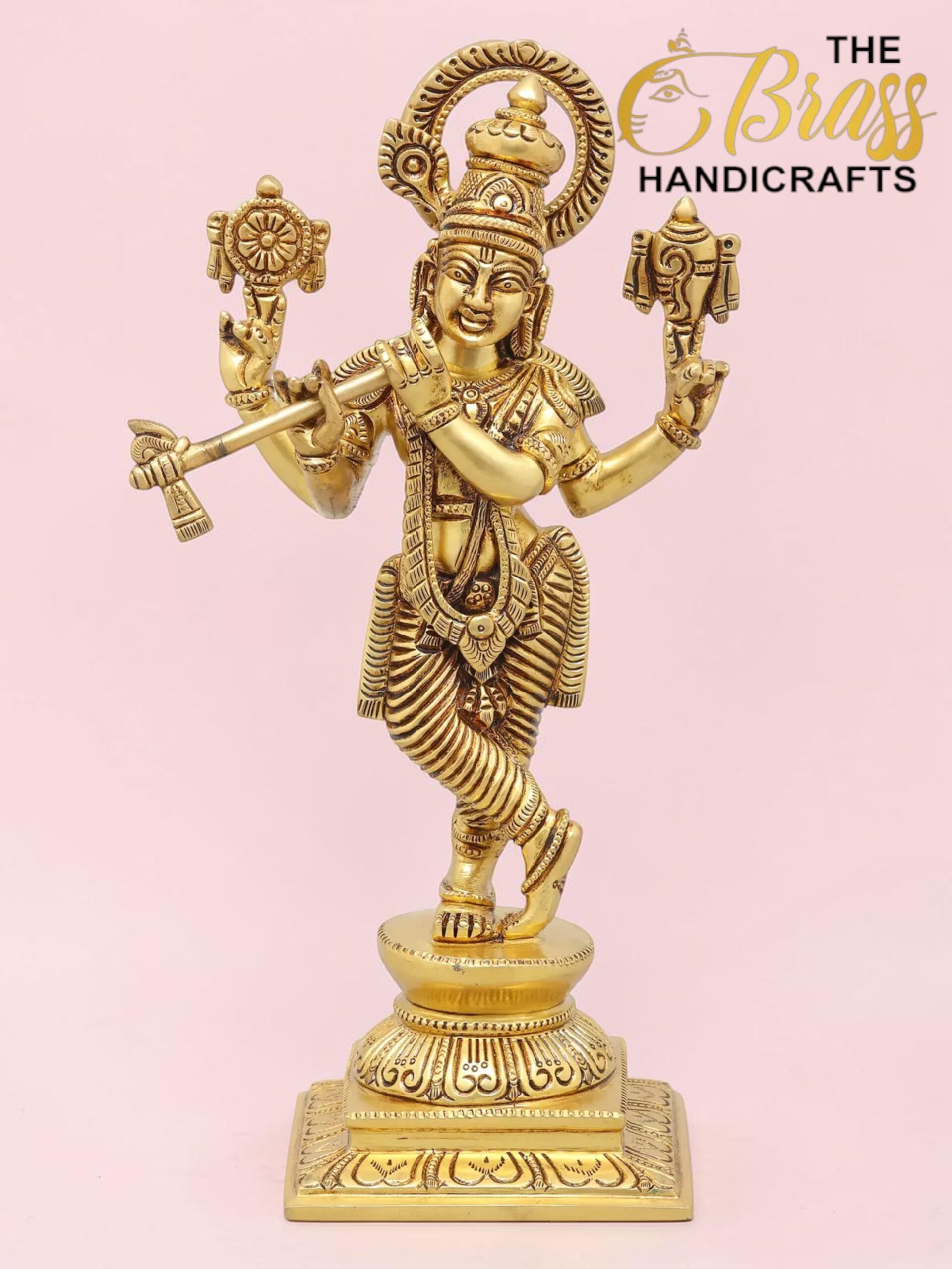 Gold-toned brass Hindu deity statue with multiple arms, ornate jewelry, standing on a pedestal against a pink background; logo 'The Brass Handicrafts' in corner.  thebrasshandicrafts.com