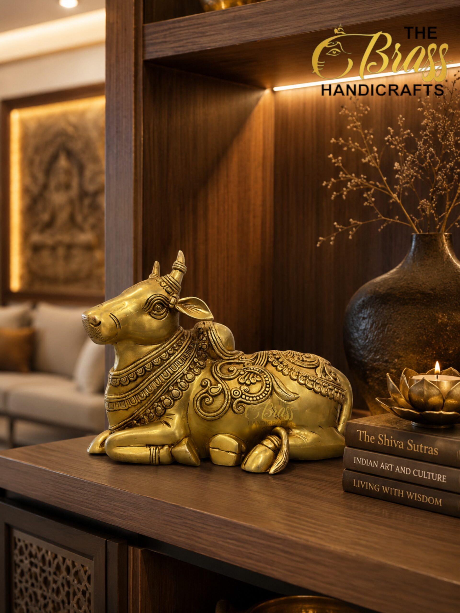 nandi 1 - thebrasshandicrafts.com Gold brass cow statue with ornate patterns on a wooden shelf, beside a dark vase and stacked books. thebrasshandicrafts.com
