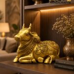 nandi 3 - thebrasshandicrafts.com Gold ornate Foo Dog statue on a dark wood shelf with warm lighting, beside dried flowers and stacked books. thebrasshandicrafts.com