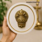 tch 1 - thebrasshandicrafts.com Hand holding a circular white display plate with a detailed gold brass ornament in the center. The Brass Handicrafts logo appears in the background. thebrasshandicrafts.com