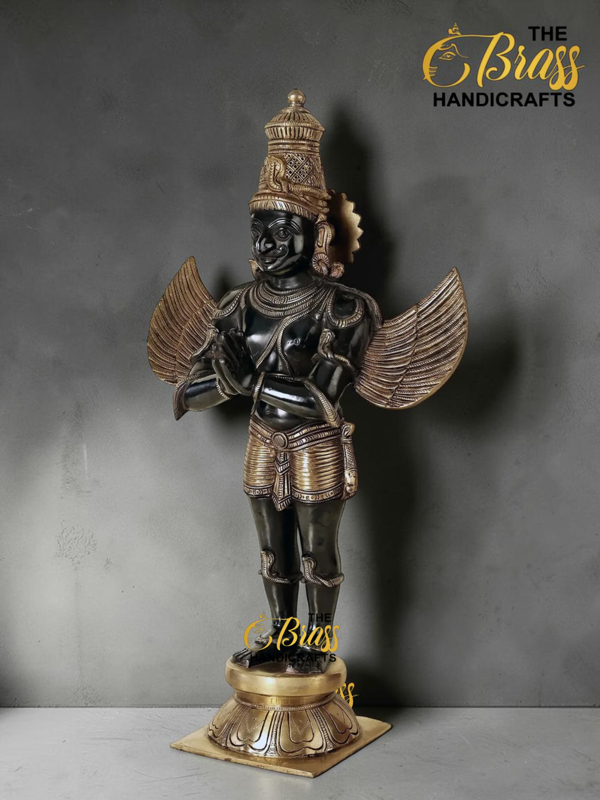 Bronze and gold statue of Garuda with detailed headdress and outstretched wings, standing on a gold pedestal (The Brass Handicrafts logo top right).  thebrasshandicrafts.com