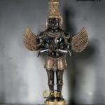 Black and gold Garuda statue with wings spread, standing on a gold pedestal, branded with The Brass Handicrafts logo and watermark in the background.  thebrasshandicrafts.com