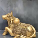 nandi 1 - thebrasshandicrafts.com Golden ornate reclining cow statue with intricate engravings and jewelry patterns, on a dark backdrop (The Brass Handicrafts watermark). thebrasshandicrafts.com