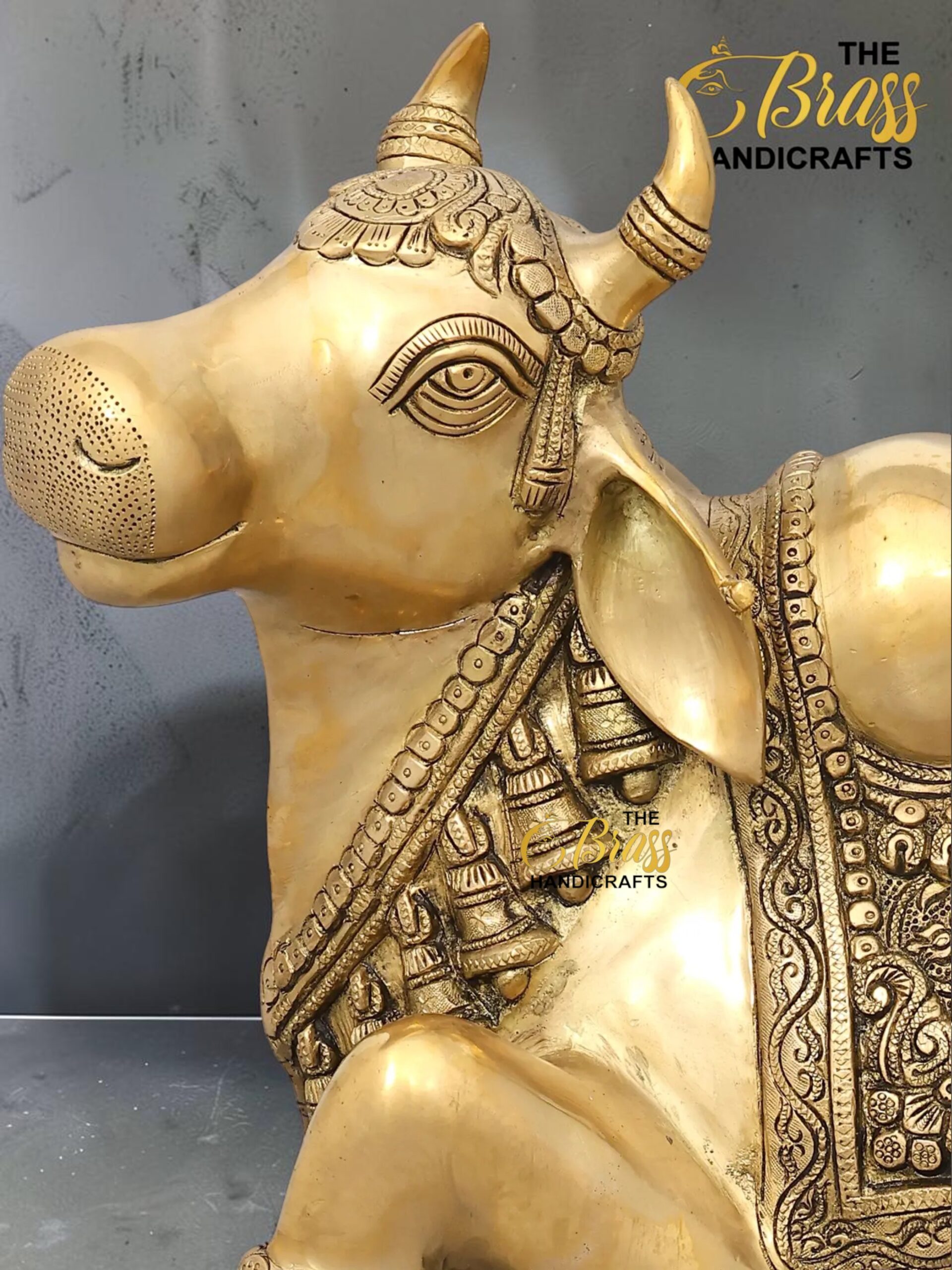 nandi 3 - thebrasshandicrafts.com Gold brass statue of a decorated Nandi bull with ornate jewelry and detailed carvings, shown in profile on a gray background. thebrasshandicrafts.com