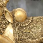 nandi 4 - thebrasshandicrafts.com Close-up of an ornate gold brass statue with detailed carvings and bead-like jewelry, with a gray background and 'The Brass Handicrafts' logo visible in the corner. thebrasshandicrafts.com