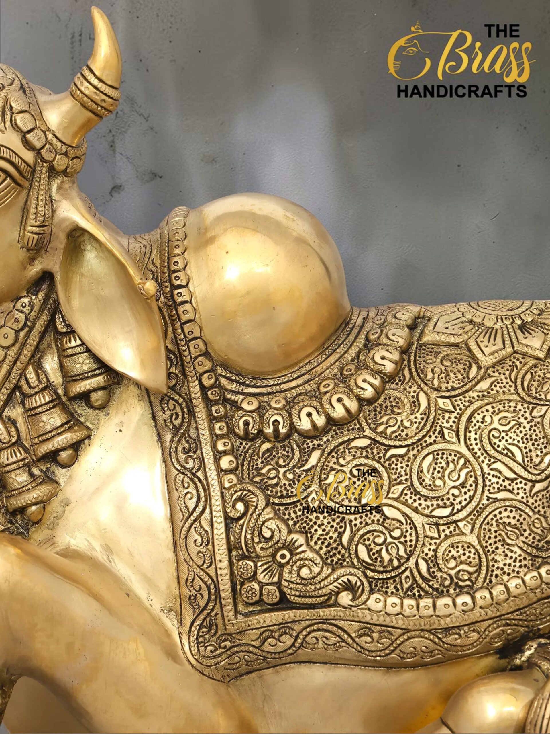 nandi 4 - thebrasshandicrafts.com Close-up of an ornate gold brass statue with detailed carvings and bead-like jewelry, with a gray background and 'The Brass Handicrafts' logo visible in the corner. thebrasshandicrafts.com