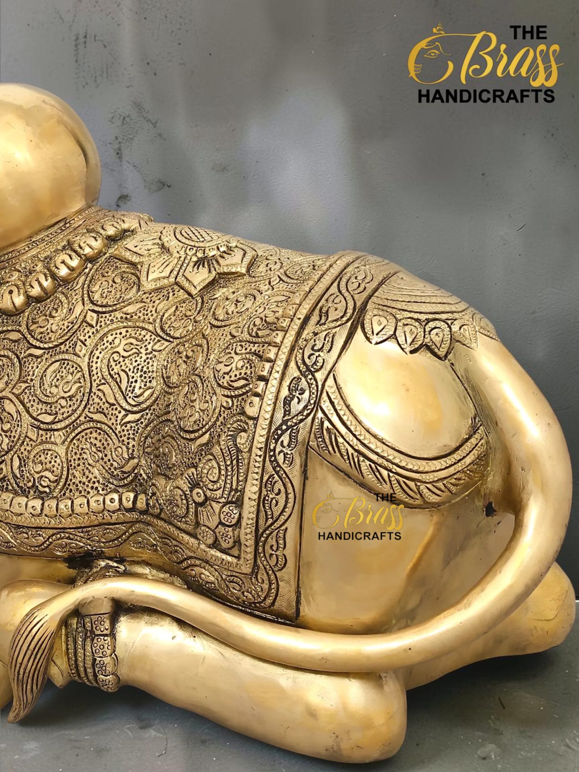 nandi 6 - thebrasshandicrafts.com Gold-toned Buddha statue with intricate carved patterns, shown reclining with a scroll-like arm; logo 'The Brass Handicrafts' visible in corner thebrasshandicrafts.com