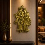 Gold-toned wall sculpture of Krishna playing a flute with Radha leaning beside him, mounted on a beige wall with warm lighting.  thebrasshandicrafts.com