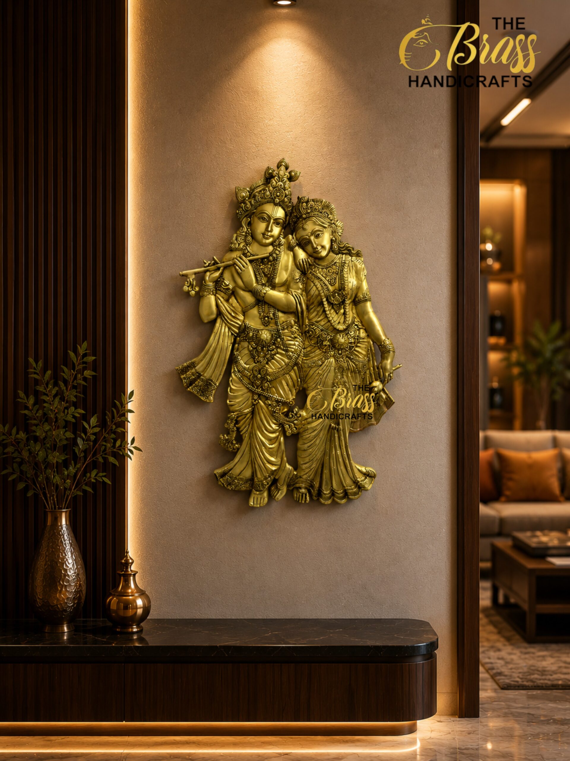 Gold-toned wall sculpture of Krishna playing a flute with Radha leaning beside him, mounted on a beige wall with warm lighting.  thebrasshandicrafts.com