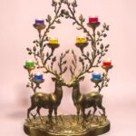 Ornate brass deer-candelabra with colorful glass votive candles on each branch against a pink backdrop.  thebrasshandicrafts.com