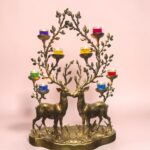 Brass candle holder shaped as two deer with colorful glass tealight cups on branching arms against a pink background.  thebrasshandicrafts.com
