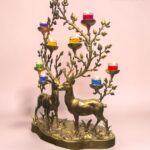 Brass deer candle tree sculpture with multicolored glass candle holders against a pink backdrop (The Brass Handicrafts logo visible).  thebrasshandicrafts.com