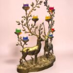 Gold-toned deer-shaped candelabra with multiple branched antlers holding small colored candles against a pink background.  thebrasshandicrafts.com