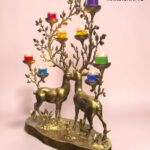 Bronze decorative candle holder featuring two deer and leafless branches with multicolored small candle cups against a pink wall.  thebrasshandicrafts.com