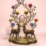Ornate brass candelabrum in the shape of two deer with tree-like branches holding small colorful candle cups against a pink background.  thebrasshandicrafts.com