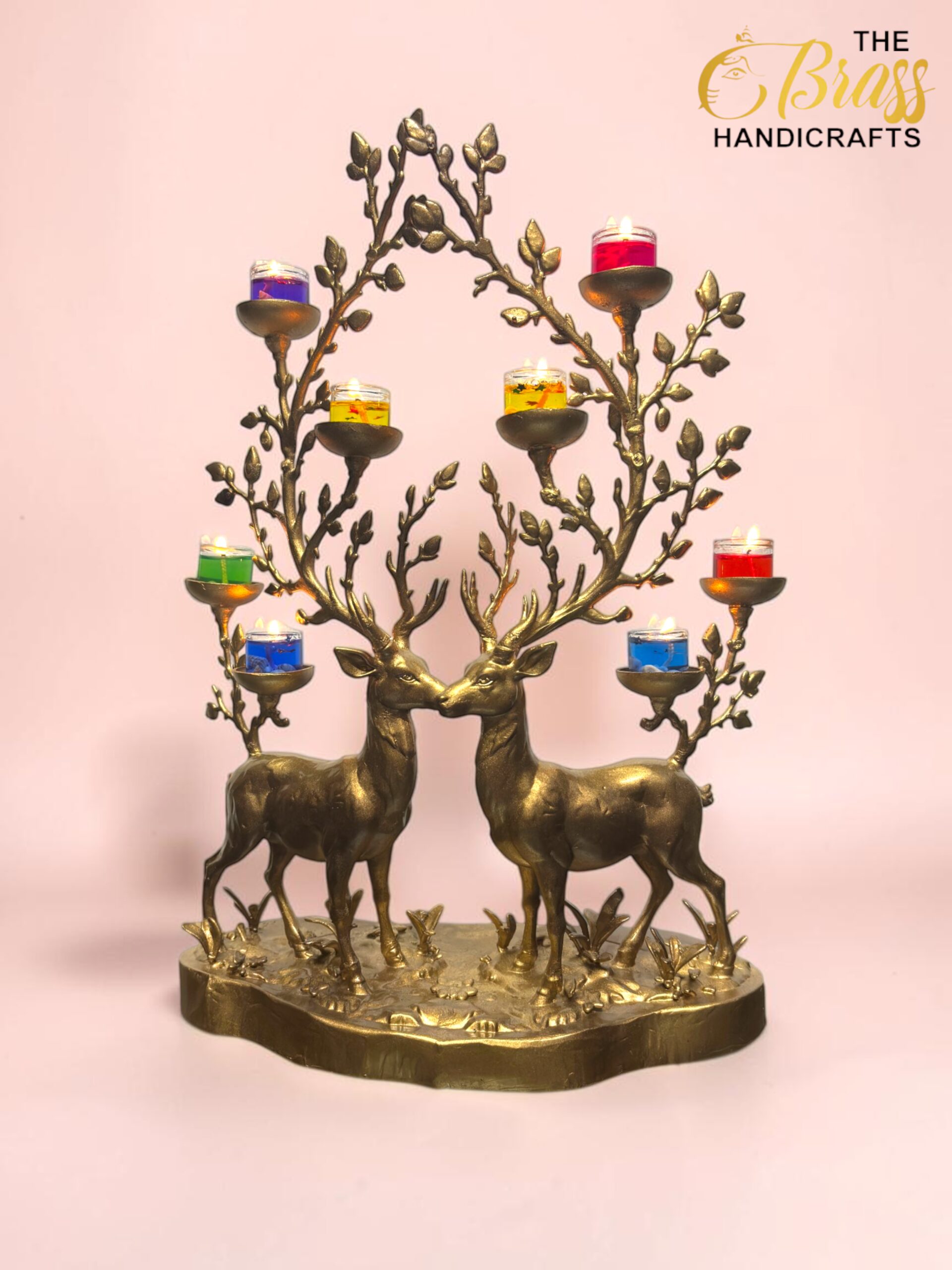 Ornate brass candelabrum in the shape of two deer with tree-like branches holding small colorful candle cups against a pink background.  thebrasshandicrafts.com