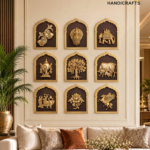 Wall display of gold relief panels with animal, tree, and nature motifs arranged in a grid on a beige wall, with a plant to the left and a sofa below.  thebrasshandicrafts.com