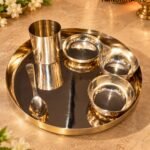 Shiny stainless steel serving set with cups and bowls on a round reflective tray, on a beige countertop with flowers in the background.  thebrasshandicrafts.com
