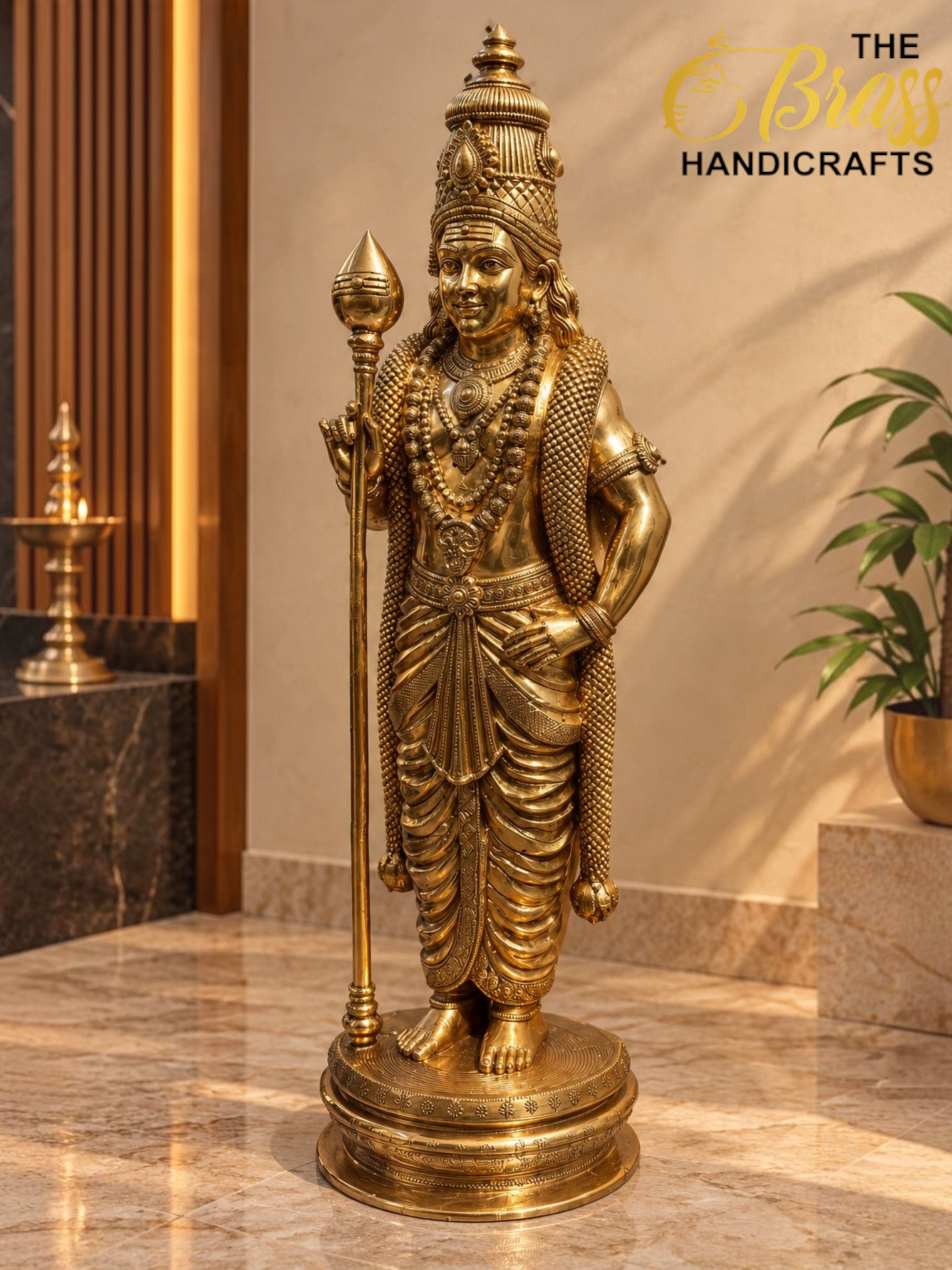 Golden Murugan Shrine in Warm Light 1 - thebrasshandicrafts.com Golden ornate statue of a Hindu deity with a tall crown, layered jewelry, and a scepter, standing on a decorative pedestal in an indoor display space. thebrasshandicrafts.com