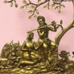 il_1588xN8446713265_ls8l - thebrasshandicrafts.com Gold-toned brass sculpture of a man playing a flute while seated on a cow under a tree against a pink background (decorative handicraft). thebrasshandicrafts.com