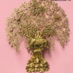 kamdhenu tree 13 - thebrasshandicrafts.com Gold-toned brass tree sculpture with dense leaves on a pink background, featuring a decorative base of circular discs; branding reads THE BRASS HANDICRAFTS. thebrasshandicrafts.com